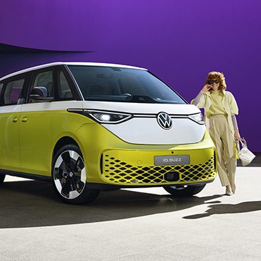 AMAG the VW ID. Buzz in white yellow, side front with woman in front of it